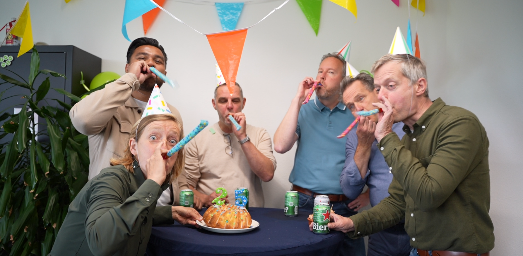 vier collega's blazen op feesttoeter en zetten taart op tafel