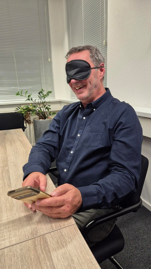 man met lapje voor ogen probeert zijn telefoon te bedienen